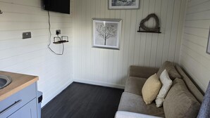 A compact living space with a kitchenette, a flat-screen TV, and two framed artworks on the wall. - Glamping Hut - Sleeps 2, hot tub & Parking (Welshpool)