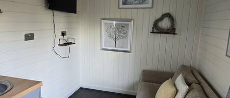 A compact living space with a kitchenette, a flat-screen TV, and two framed artworks on the wall.