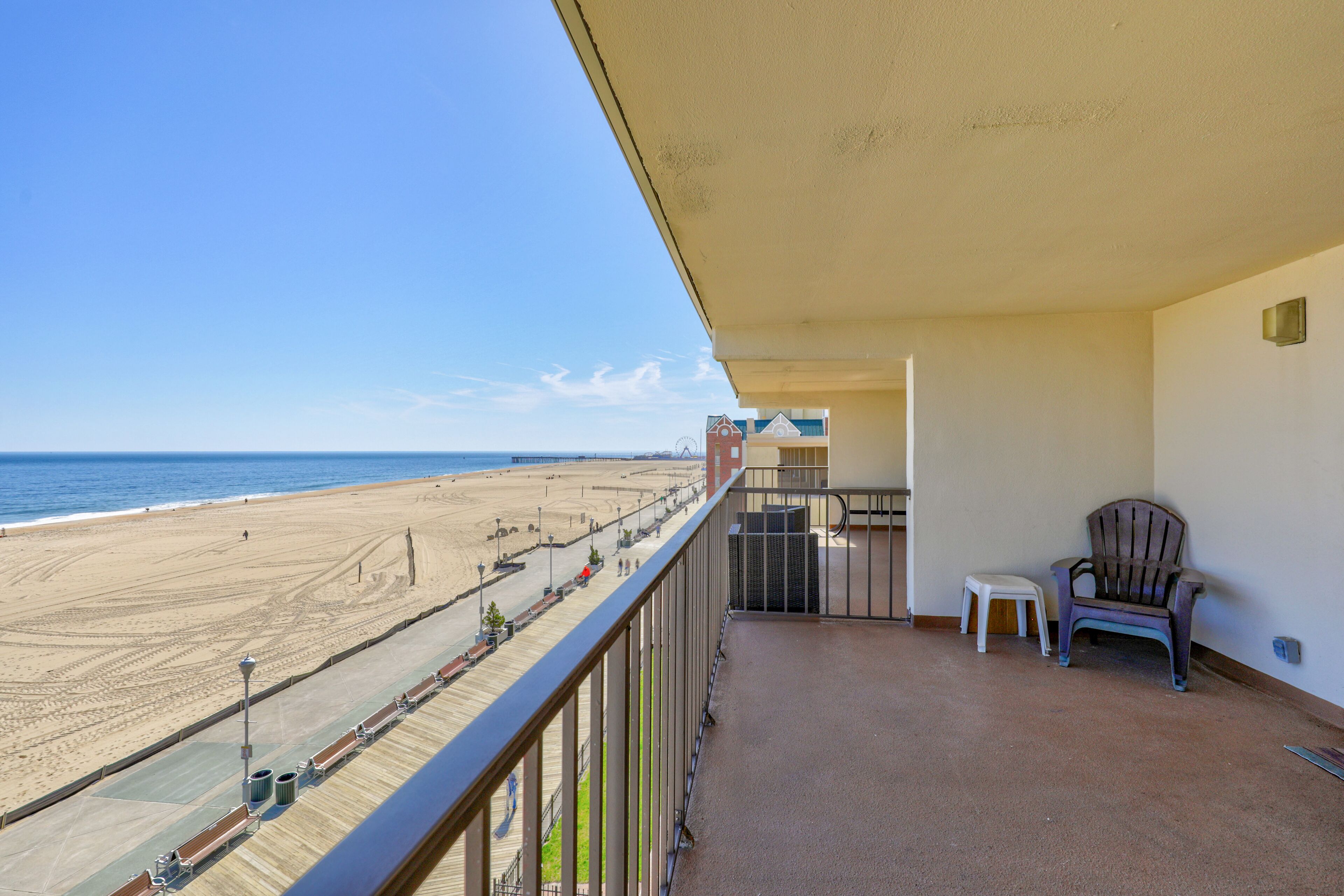 A balcony with a view of the beach, a chair, and a small table.