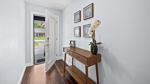 Een hal met een houten console tafel, een vaas met bloemen en ingekaderde foto's aan de muur.