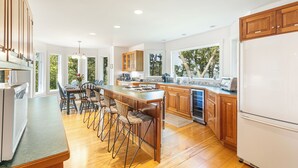 A modern kitchen with wooden cabinets, a central island with bar stools, a built-in oven, and a large window providing a view of trees. - A View Fit for Royalty!
Top Compliments:  so clean! fab hot tub! best view! (Tisbury)