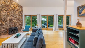 A spacious living room with a stone wall, a fireplace, a sofa, and a large window with a view of greenery. - A View Fit for Royalty!
Top Compliments:  so clean! fab hot tub! best view! (Tisbury)