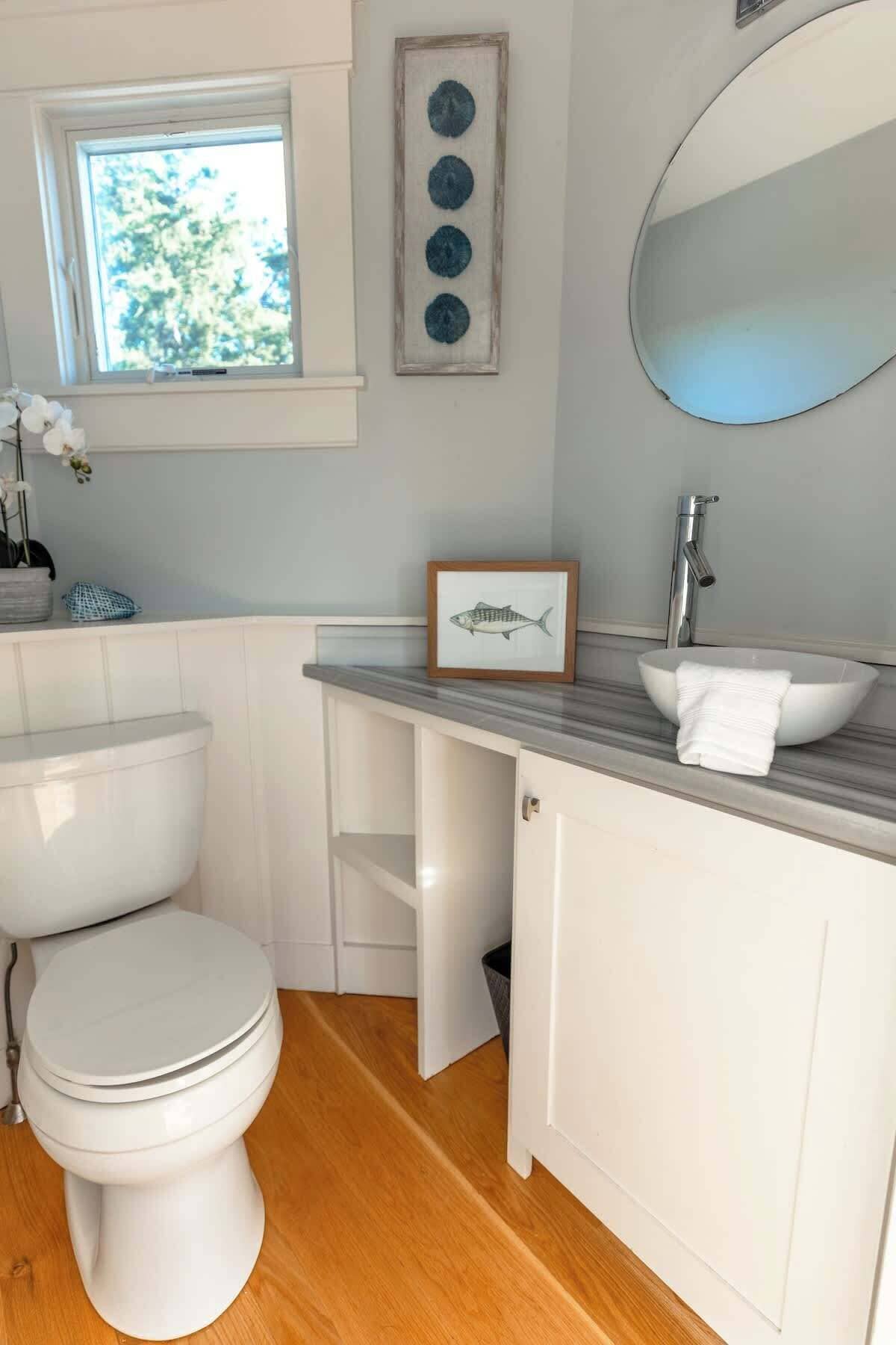 Une salle de bain comprenant des toilettes, un lavabo avec un bac, un miroir et un tableau encadré représentant un poisson.