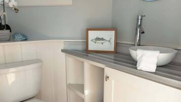 A bathroom with a toilet, a sink with a basin, a mirror, and a framed picture of a fish.