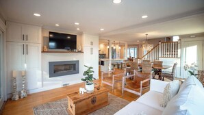 A spacious living room with a fireplace, a television mounted above it, and a staircase leading to an upper level. - Luxury Waterfront Property 360 water views (Portsmouth)