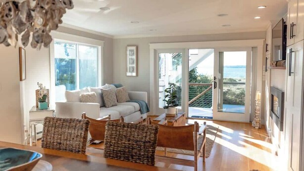 A modern living room with a sofa, chairs, and a dining table. There is a large window with a view of the outdoors. - Luxury Waterfront Property 360 water views (Portsmouth)