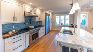 A modern kitchen with white cabinets, a blue backsplash, stainless steel appliances, and a large island with a sink. - Luxury Waterfront Property 360 water views (Portsmouth)