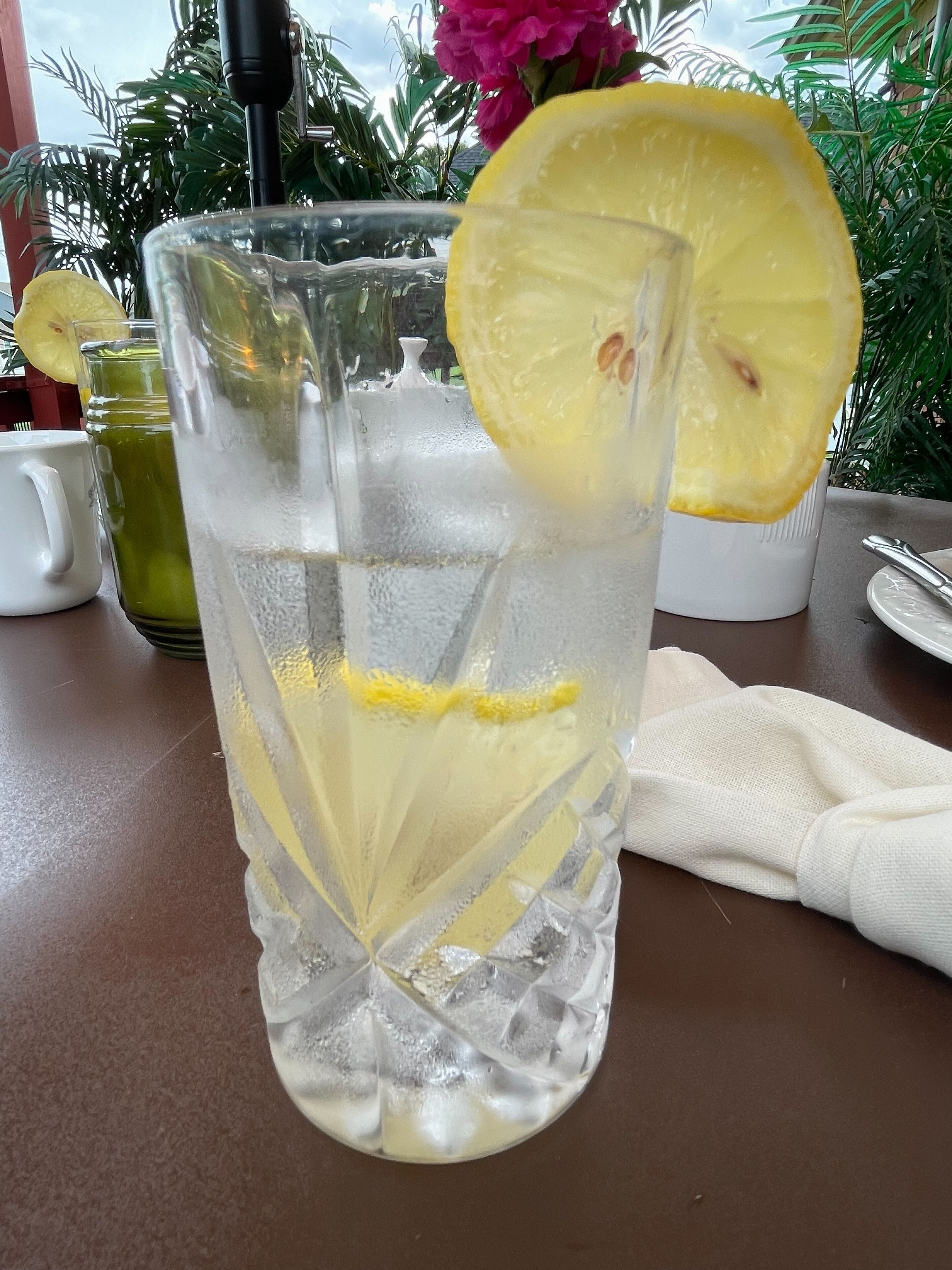 Un vaso de agua con una rodaja de limón, una jarra y una taza sobre una mesa.
