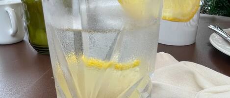 Un vaso de agua con una rodaja de limón, una jarra y una taza sobre una mesa.