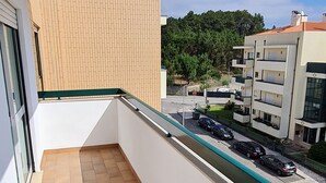 Parvekkeessa on laatoitettu lattia, lasiovi ja sieltä avautuu näkymä parkkialueelle ja taustalla näkyville rakennuksille.
