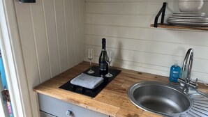 A compact kitchen with a sink, a wine bottle, and glasses on a black mat. - Cabin - Sleeps 2 hot tub & Parking (Welshpool)