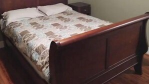 Un lit simple avec un cadre en bois et une couvre-lit à motifs, dans une pièce dotée d’un plancher en bois et d’un mur vert.