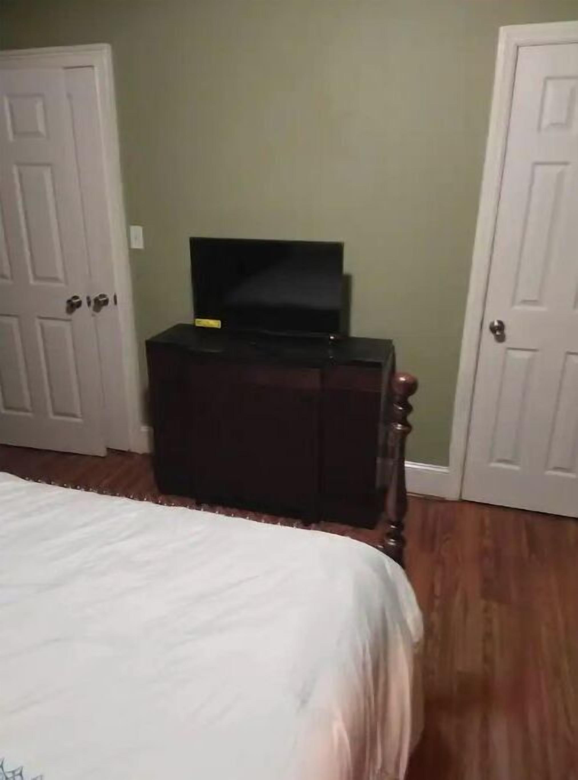 A bedroom with a bed, a dresser, and a television on top of it. There are two doors visible in the room.