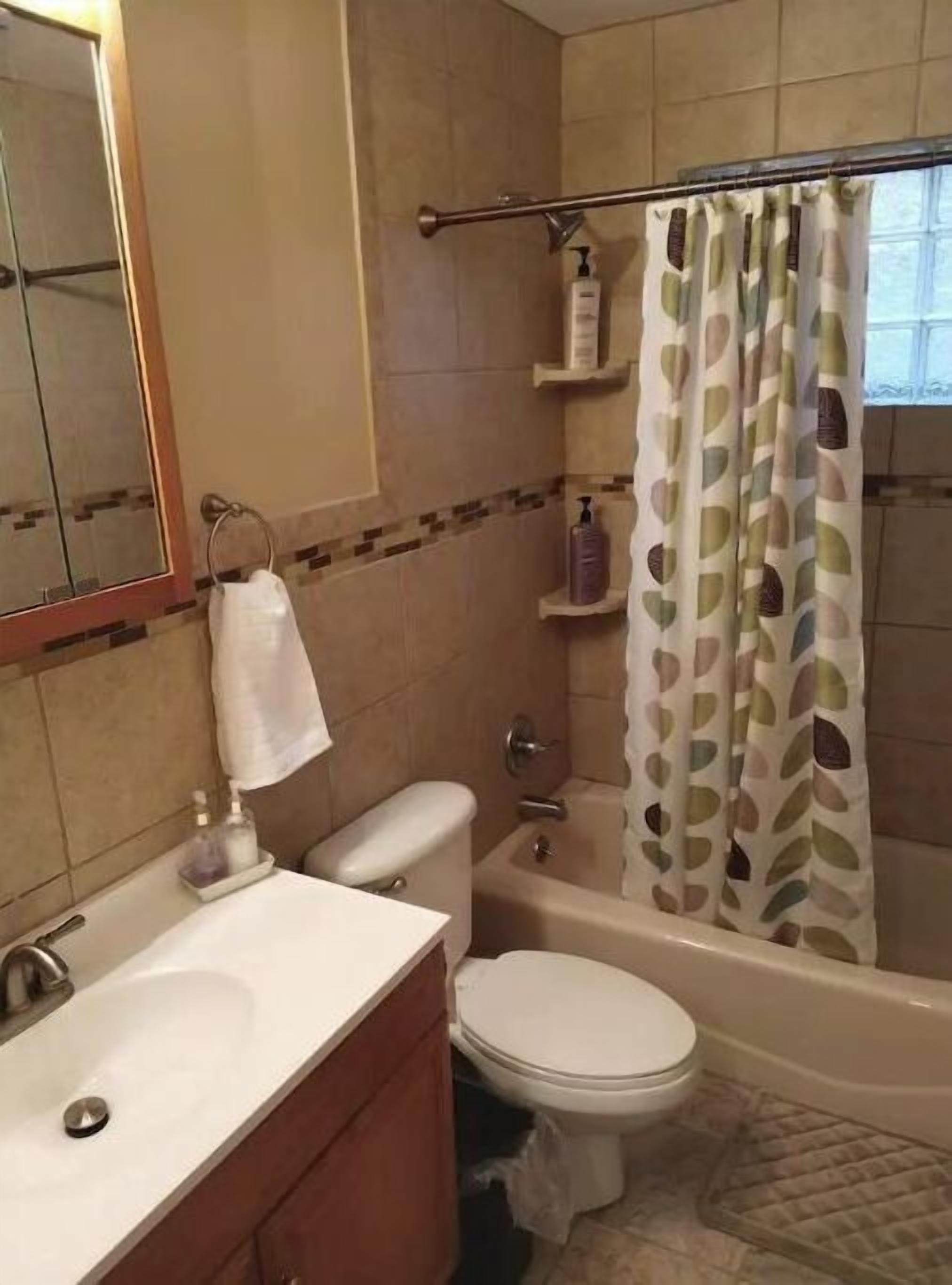 A bathroom with a sink, toilet, and bathtub. There is a towel hanging on the wall and a shower curtain with a leaf pattern.