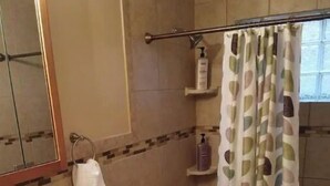 Une salle de bain avec un lavabo, des toilettes et une baignoire. Une serviette est accrochée au mur et il y a un rideau de douche orné d’un motif de feuilles.