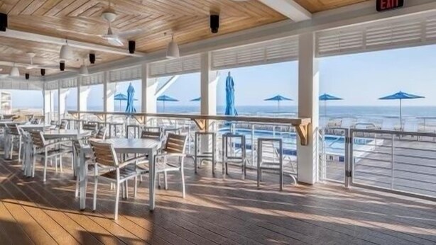 Un espace extérieur abrité, aménagé pour les repas, avec des tables, des chaises, de grandes fenêtres et des parasols.