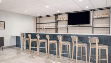 A bar area with a long counter, multiple bar stools, and shelves with bottles.