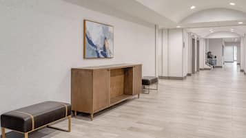A spacious hallway with a wooden bench and a cabinet, a painting on the wall, and a staircase in the distance.