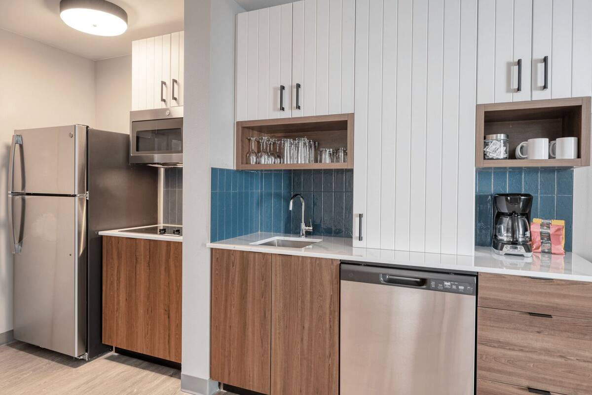 A modern kitchen with stainless steel appliances, wooden cabinets, and blue-tiled backsplash.