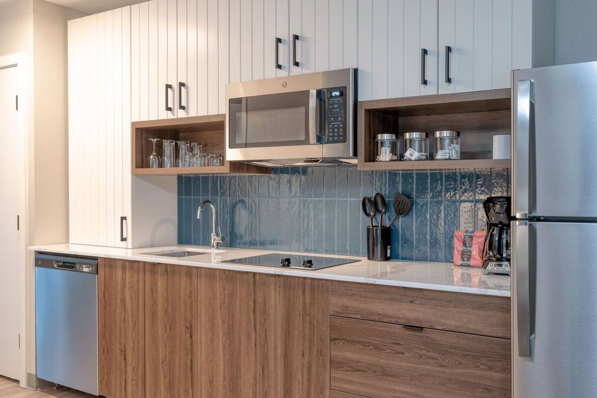 A modern kitchen with wooden cabinets, a stainless steel refrigerator, a microwave, and a sink.