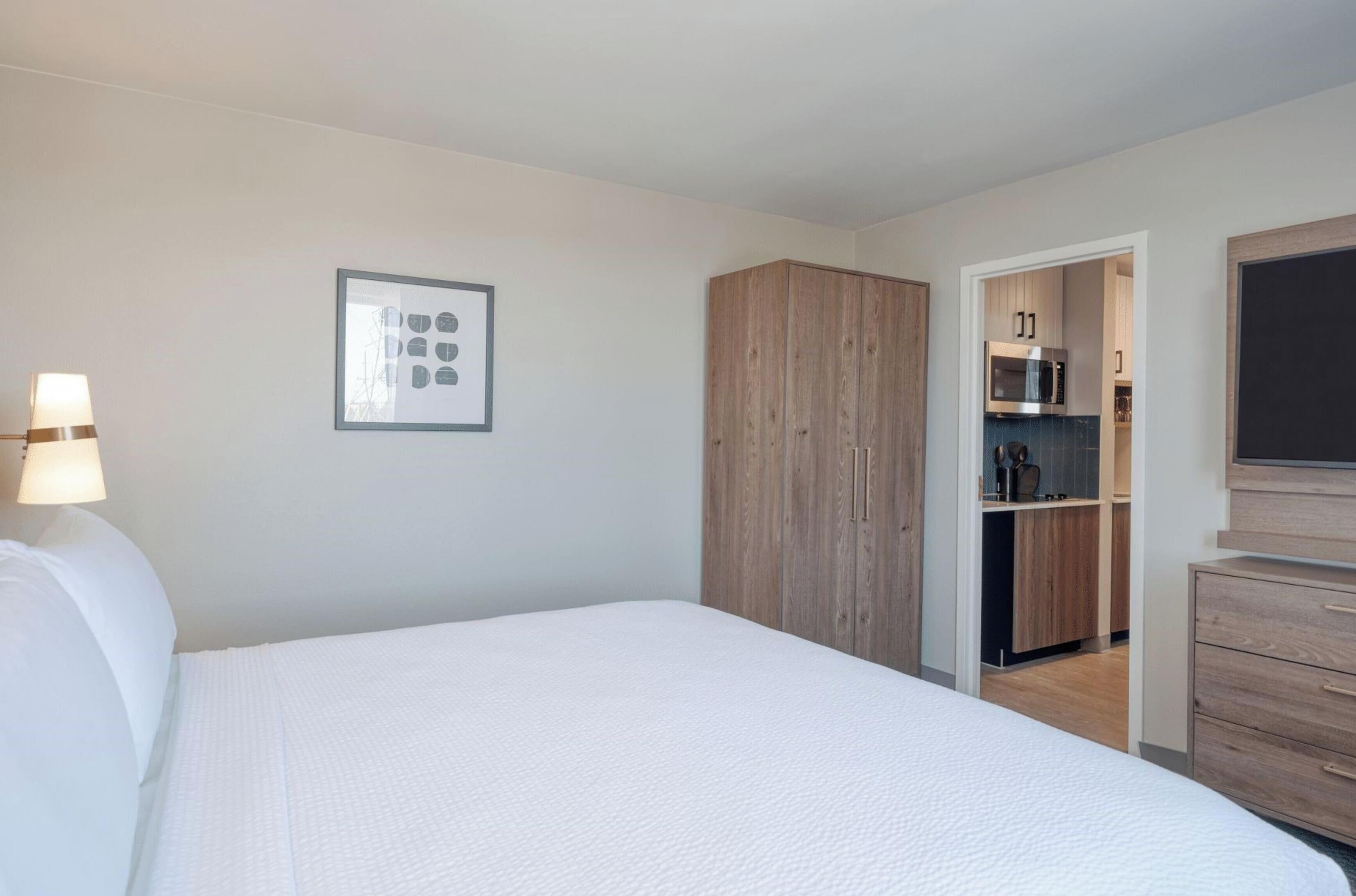 Une chambre avec un lit, une armoire en bois, une autre armoire contenant un four à micro-ondes et un téléviseur.
