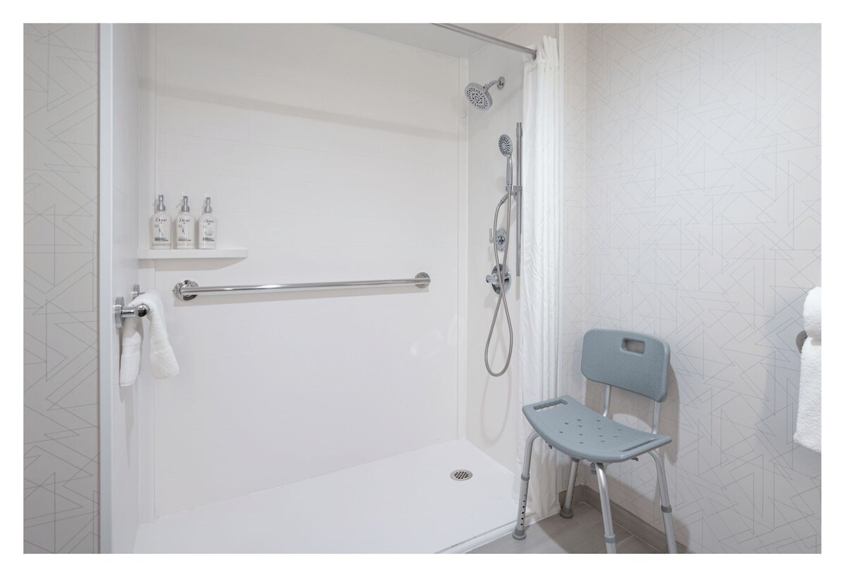 A walk-in shower with a grab bar, a shower chair, and a shelf with toiletries.