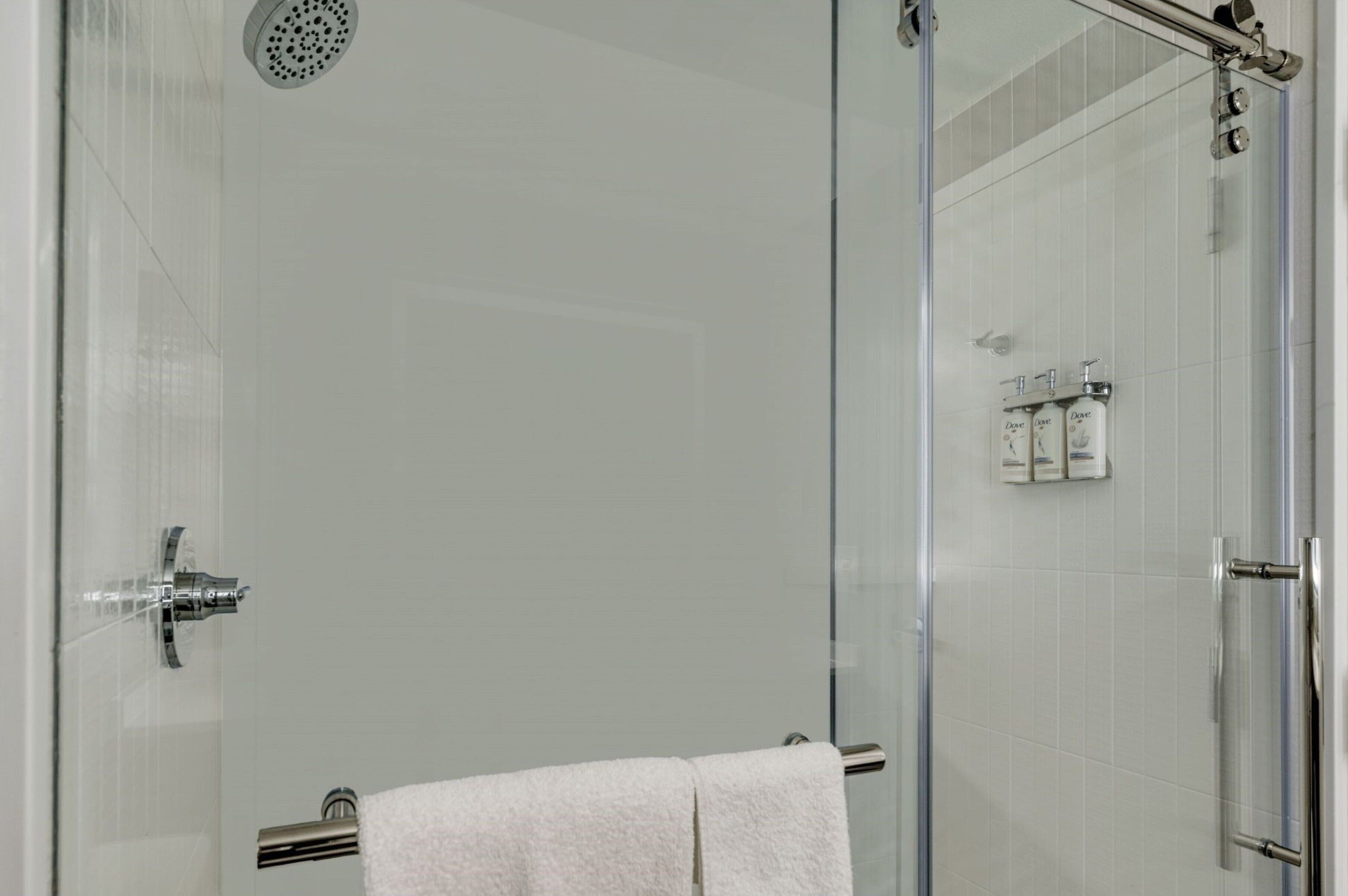 A glass-enclosed shower with a handheld showerhead, a glass door, and a towel rack with a white towel.