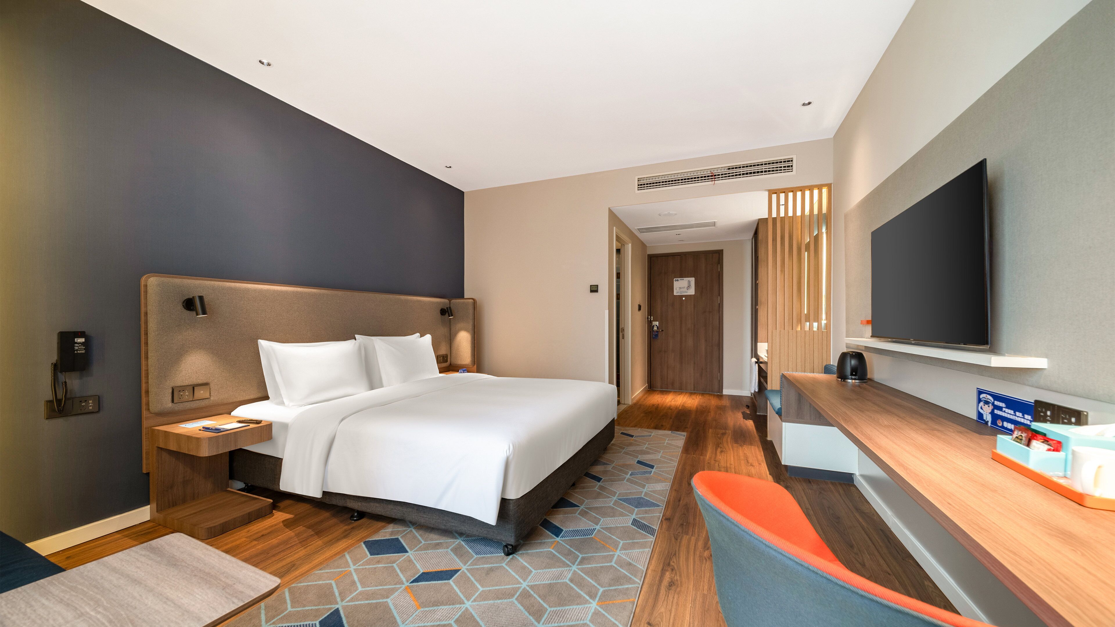 Una habitación de hotel con cama, mesita de noche, televisor y escritorio.