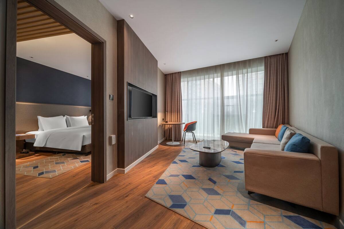 Ein modernes Hotelzimmer mit Bett, Sofa, Couchtisch und Fernseher.