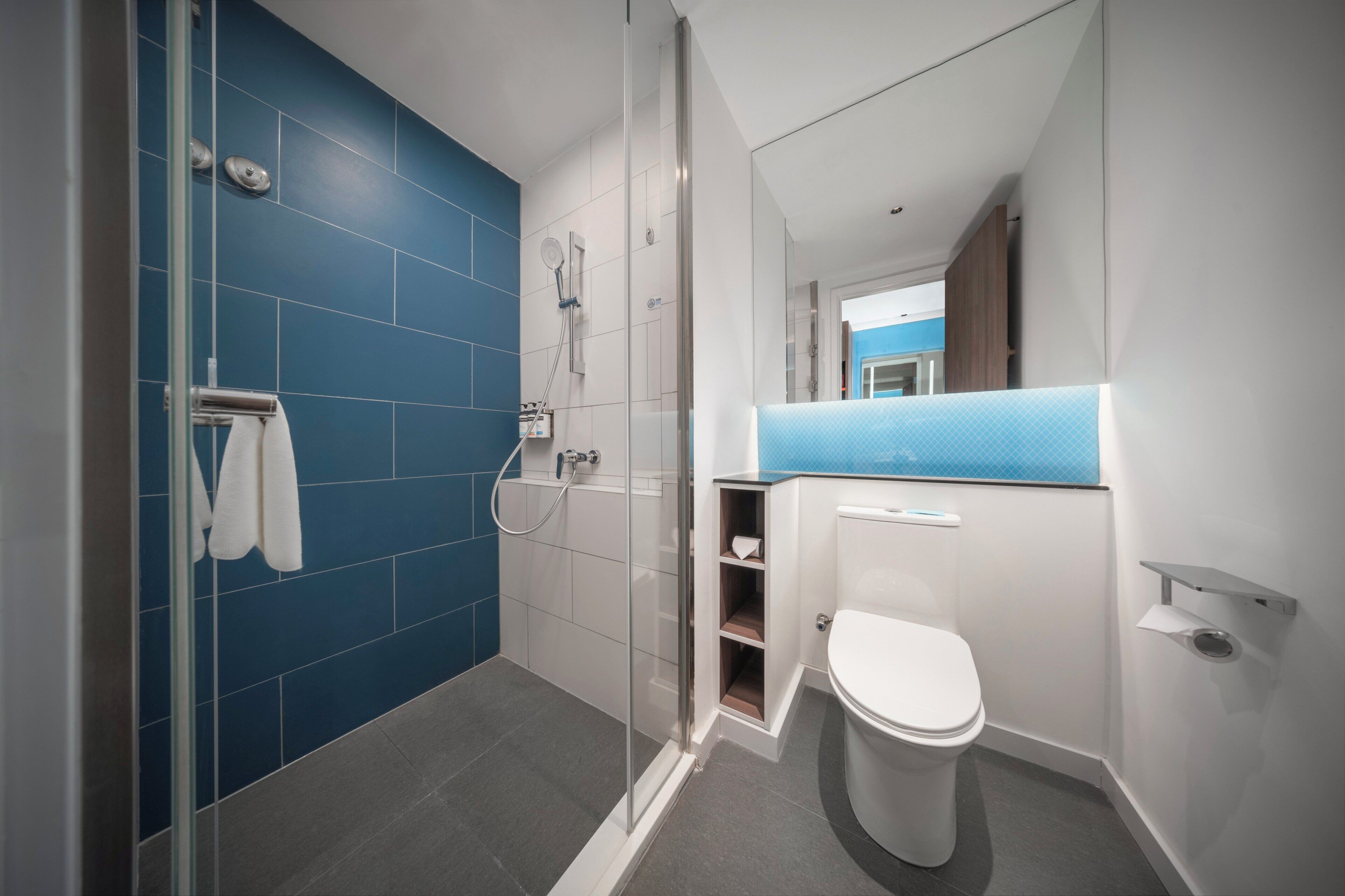 A modern bathroom with a glass-enclosed shower, a white toilet, and a blue-tiled wall.