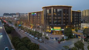 Un hotel Holiday Inn Express con un diseño moderno, situado cerca de una calle concurrida, con coches y una acera para peatones.