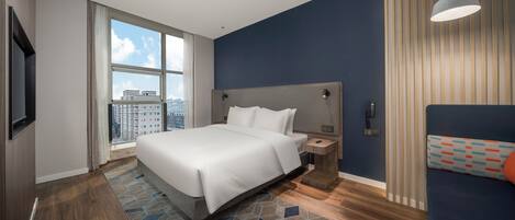 Una habitación de hotel moderna con una cama grande, una mesita de noche, un televisor y vistas a la ciudad.