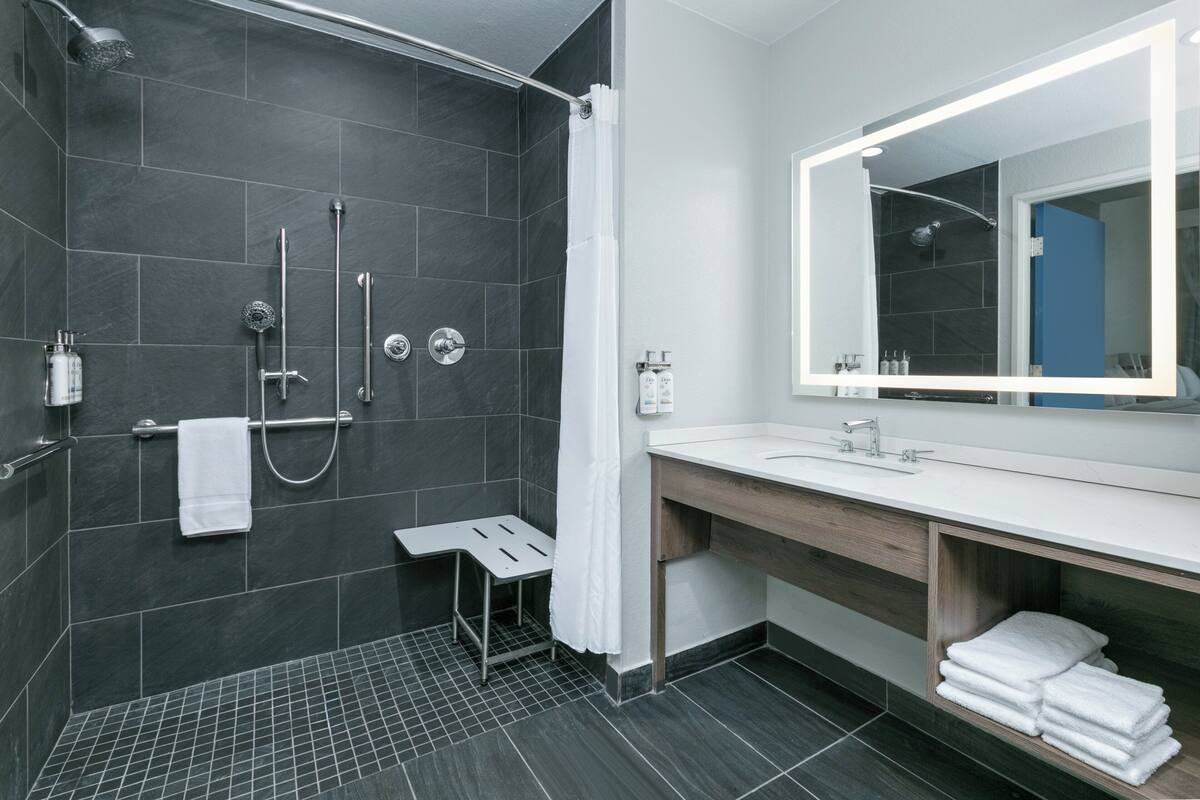 Ein modernes Badezimmer mit einer dunklen Duschkabine, einem weißen Waschbecken und einer Holz-Waschplatzkonsole sowie einem großen Spiegel.