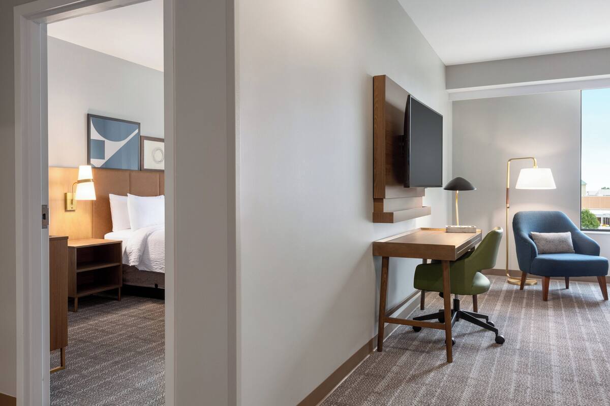 Ein Hotelzimmer mit Bett, Schreibtisch, Stuhl, Fernseher und Blick ins Freie.
