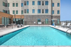 A rectangular swimming pool with a clear blue water, surrounded by a black metal fence. There are lounge chairs and umbrellas on the poolside. - Staybridge Suites San Antonio Lackland AFB Area by IHG (San Antonio)