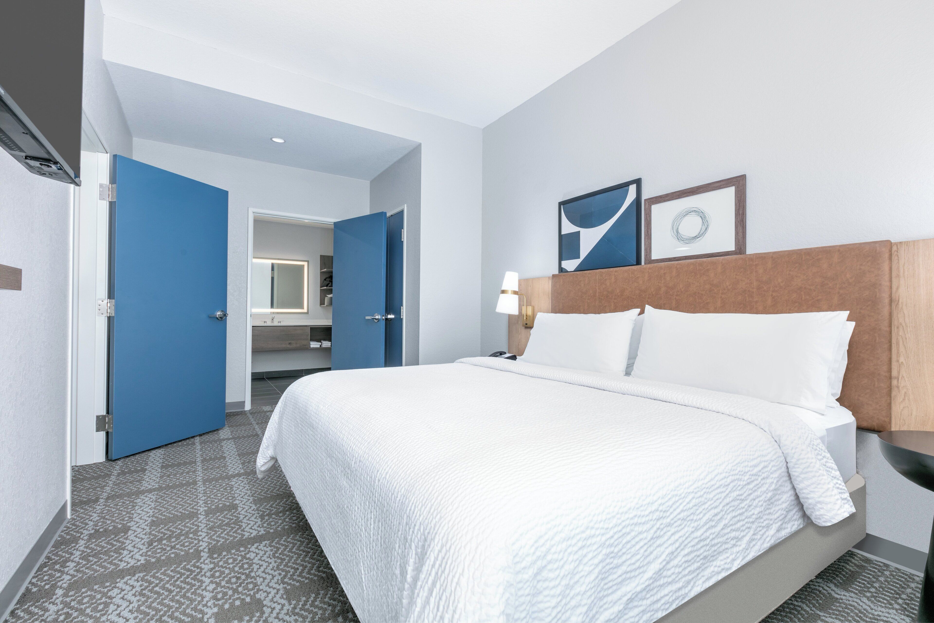 Habitación de hotel con una cama grande, una mesita de noche, una puerta azul y un baño visible a través de una puerta abierta.