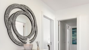 Un couloir avec un plancher en bois, un comptoir d’accueil blanc, un grand miroir et un tableau accroché au mur.