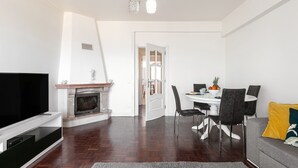 Un salon moderne doté d’un téléviseur à écran plat, d’une cheminée, d’un coin repas avec une table et des chaises, et d’un canapé gris.