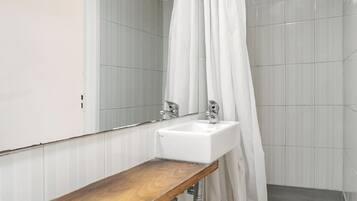 Een moderne badkamer met een houten plank, een witte wastafel, een douche met gordijn en betegelde wanden.