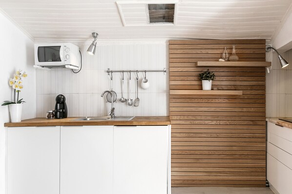 A kitchen with white cabinets, a wooden countertop, a microwave, a coffee maker, hanging utensils, and a potted plant.