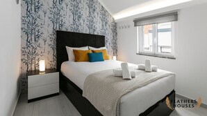 A modern bedroom with a bed, bedside table, and a window. - Beach Alley Apartment (Nazaré)