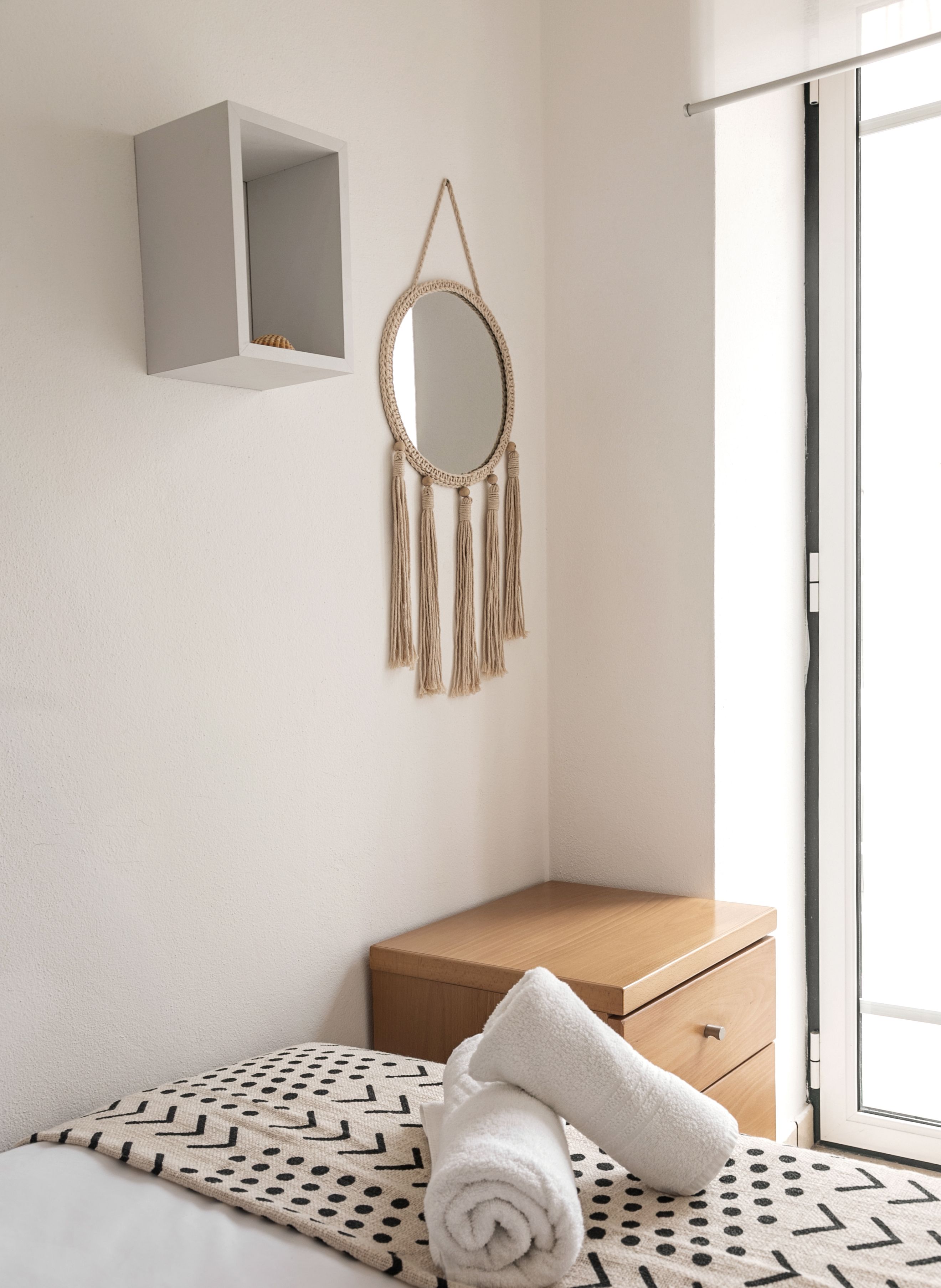 Een slaapkamer met een bed, nachtkastje, spiegel en een wandplank.