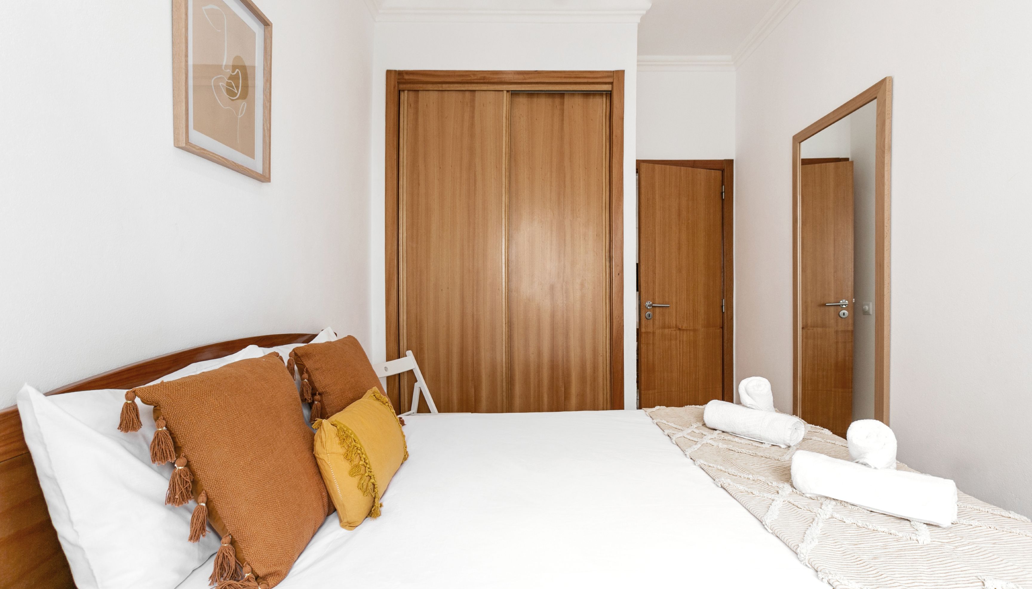 A bedroom with a large bed, wooden wardrobe, and a mirror.