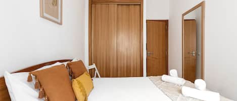 A bedroom with a large bed, wooden wardrobe, and a mirror.