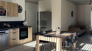 Cocina moderna con armarios de madera, horno empotrado y microondas. Cuenta con un comedor con mesa y sillas de madera, y un ventilador de techo.