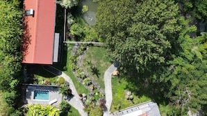 Vista aérea de una zona residencial con dos casas de tejados rojos, una piscina y un pequeño estanque rodeado de abundante vegetación.