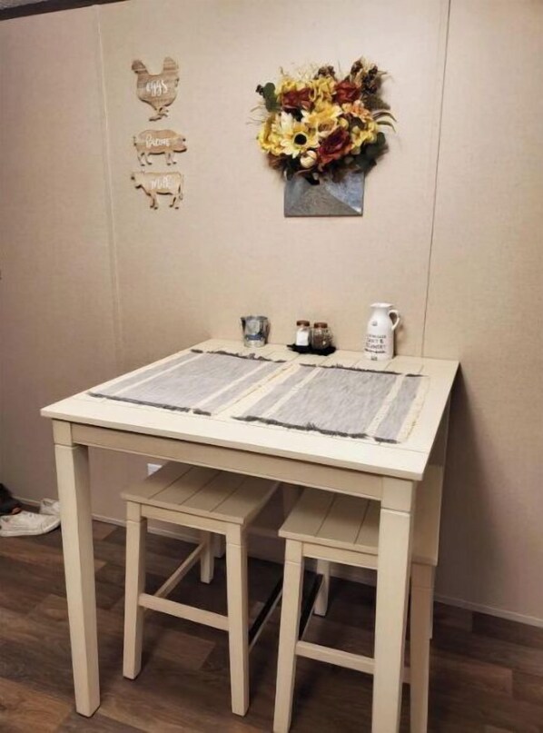 A small dining table with a placemat, two chairs, a decorative wall hanging, and a small vase with dried flowers. - Peaceful country home away in the wilderness (Galena)