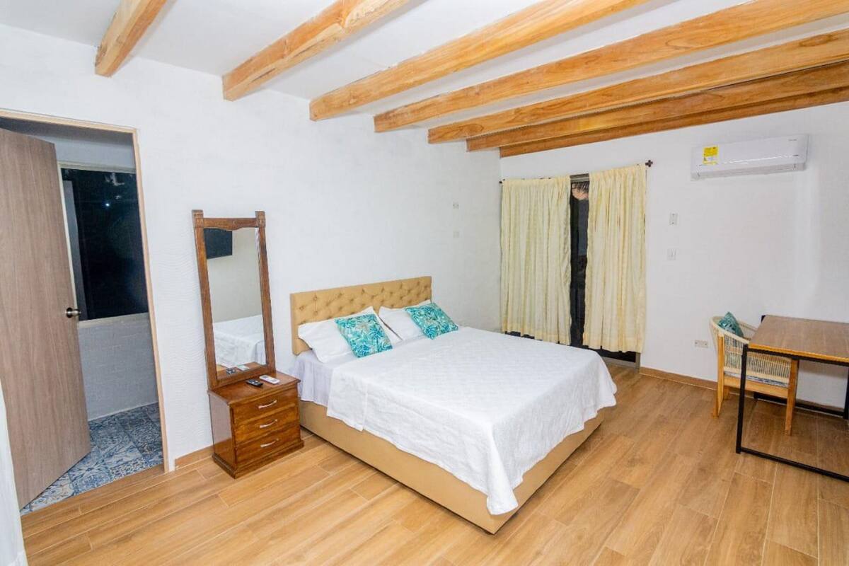 Une chambre avec un plafond en bois, un lit avec une literie blanche, une commode en bois et une petite table.