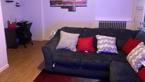 A living room with a grey sofa, red and patterned cushions, a black office chair, a small desk, and a wall-mounted abstract art piece. - Cozy apartment steps from Christ Hospital, UC and minutes to downtown! (Cincinnati)