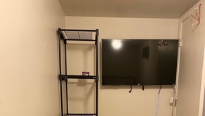 A small, narrow room with a bed, a TV mounted on the wall, and a metal shelf unit against the wall. - Cozy apartment steps from Christ Hospital, UC and minutes to downtown! (Cincinnati)